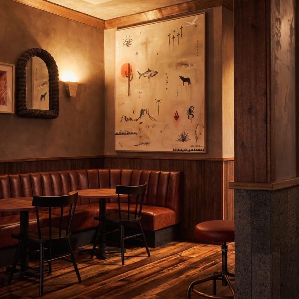 Warmly lit restaurant dining area with leather booths, wooden tables, stools, framed artwork, and rustic wood-paneled decor.