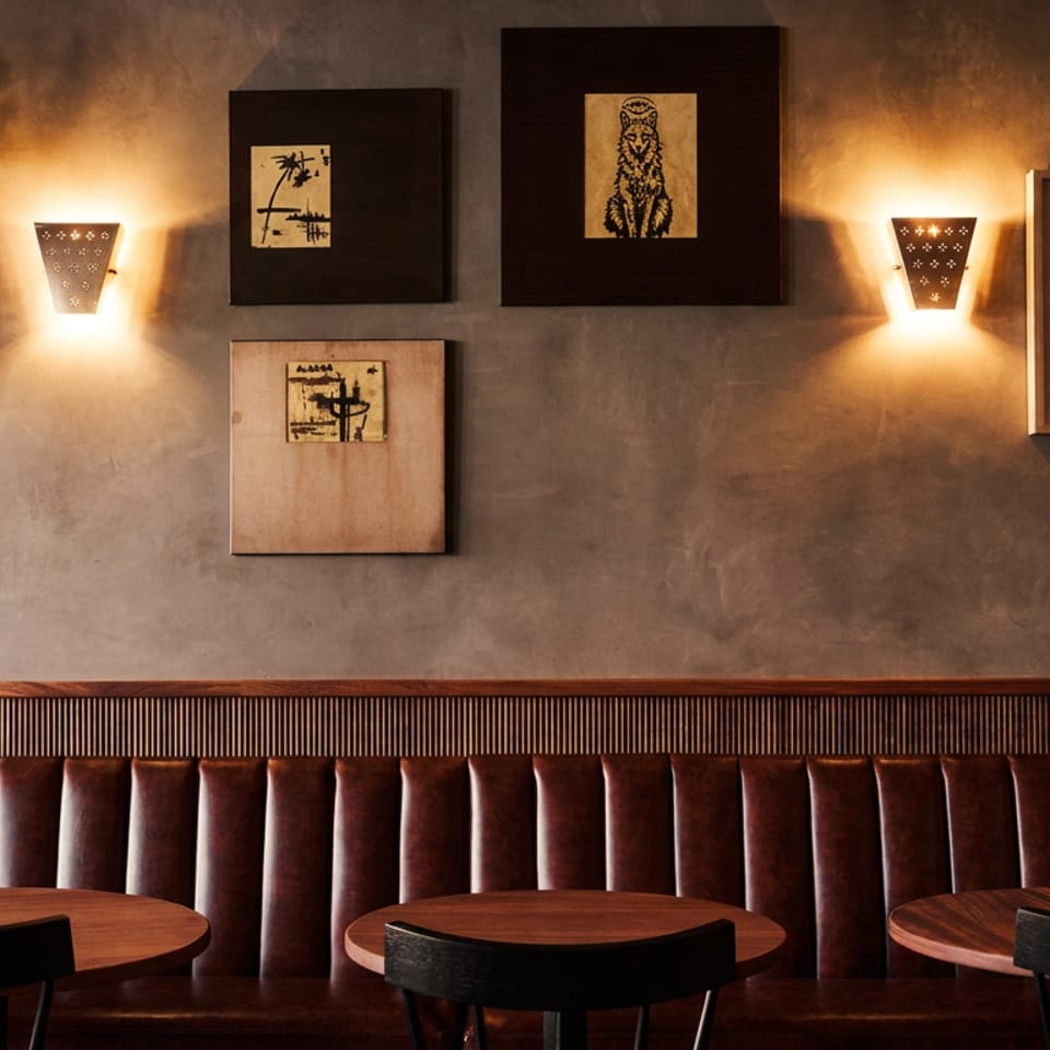 Warmly lit restaurant interior with leather booth seating, wooden tables, wall sconces, and framed artwork.