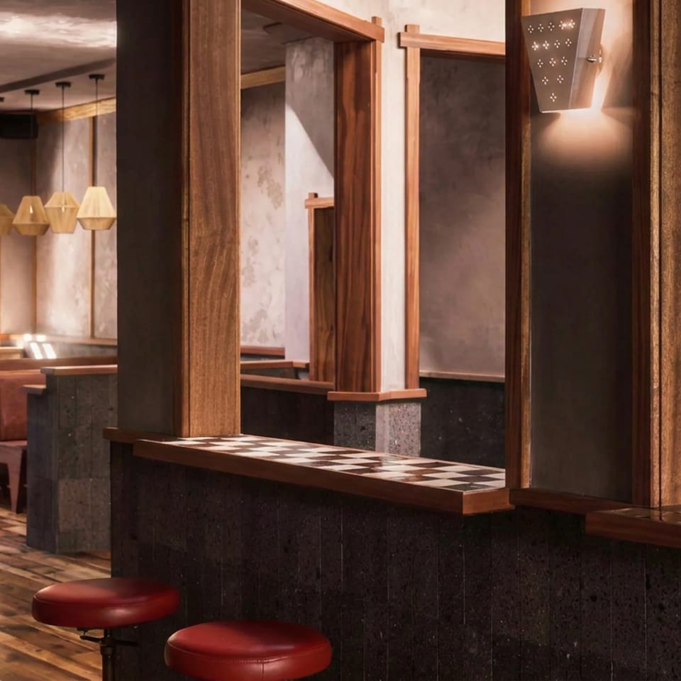 Warmly lit restaurant interior with wood paneling, checkerboard counters, red stools, booths, and pendant lights.
