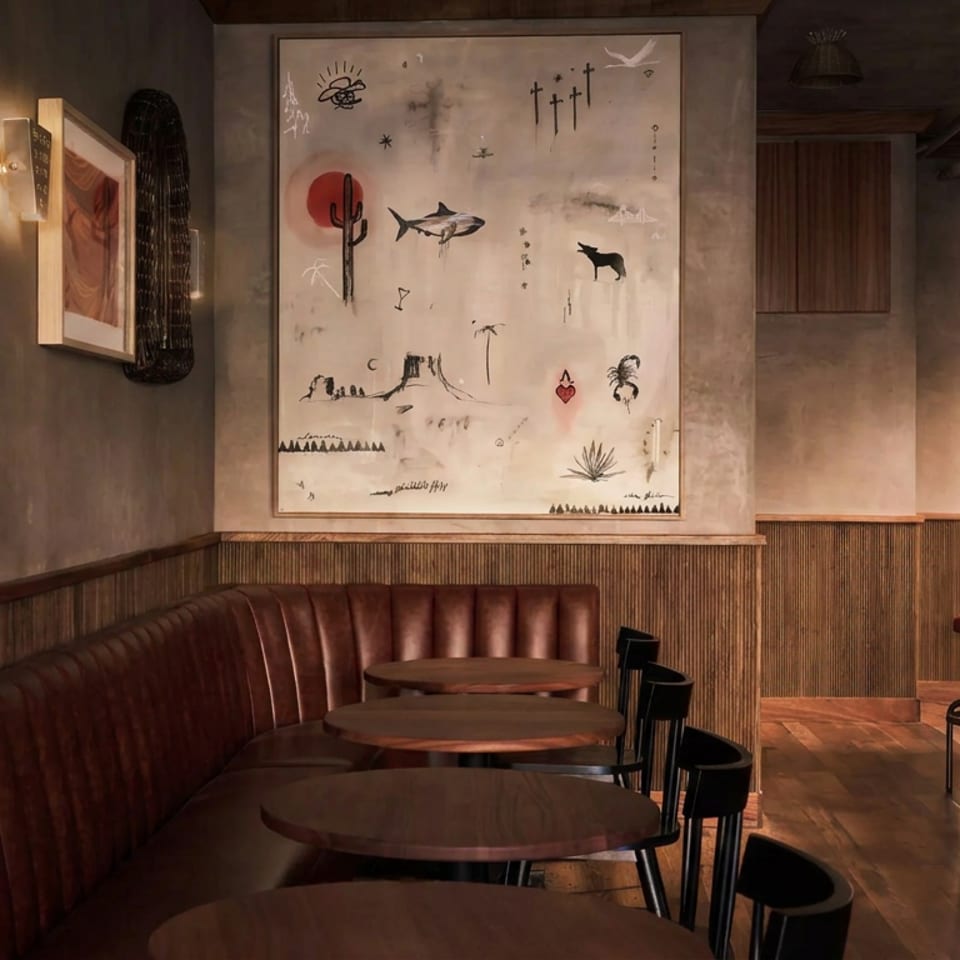Warmly lit restaurant interior with leather booth seating, round wooden tables, bar stools, and Southwestern-inspired artwork.