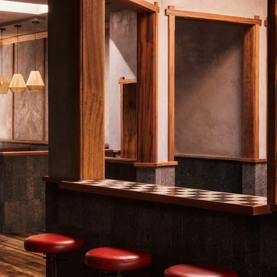 Warmly lit restaurant interior with wood-framed openings, red stools, checkerboard counters, pendant lights, and exposed textured walls.