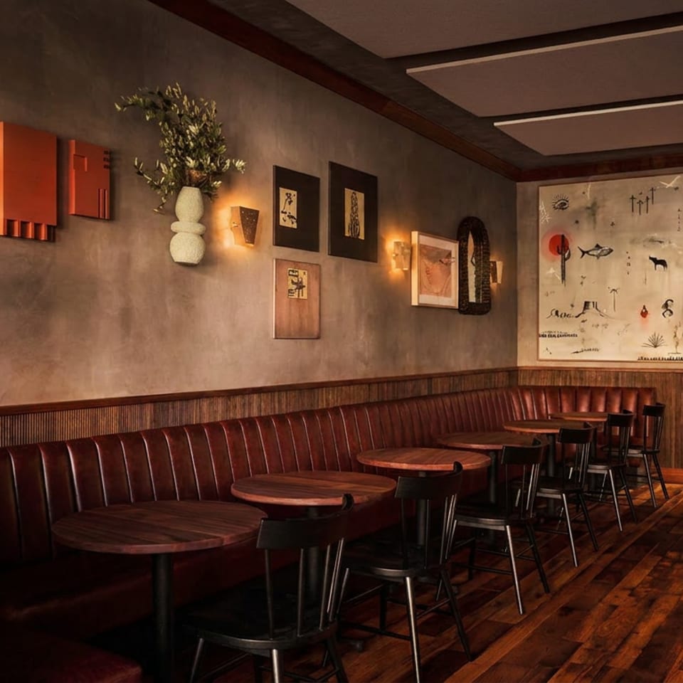 Warmly lit restaurant dining room with leather booths, round wooden tables, bar stools, wood flooring, and eclectic wall art.